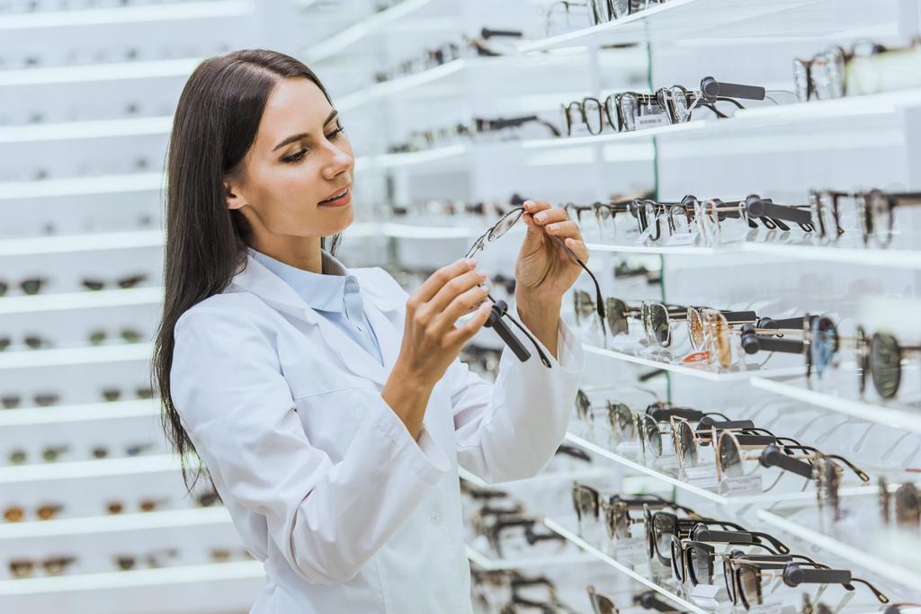 Szemüvegek közelében polcok szemészeti üzletben nézett gyönyörű optometrista - Fotó, kép