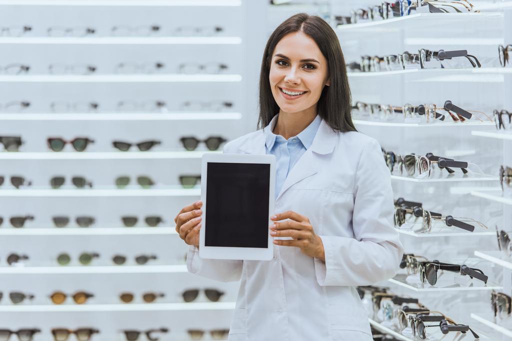 opticien souriant attrayant montrant tablette numérique avec écran blanc dans la boutique ophtalmique
 - Photo, image