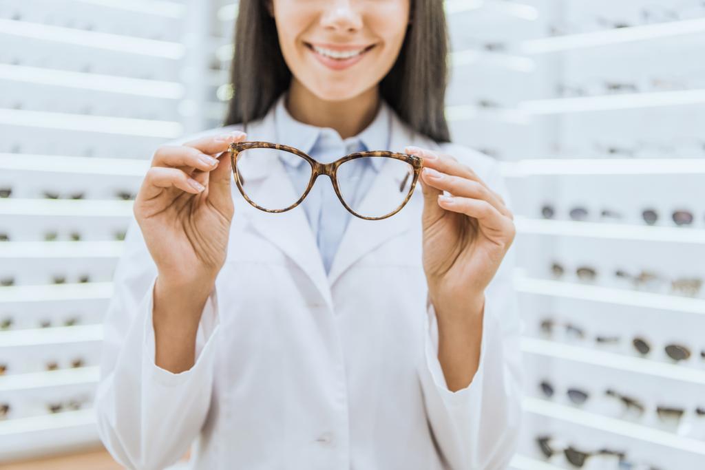 обрізаний вид усміхненого професійного окуляра, що тримає окуляри
 - Фото, зображення