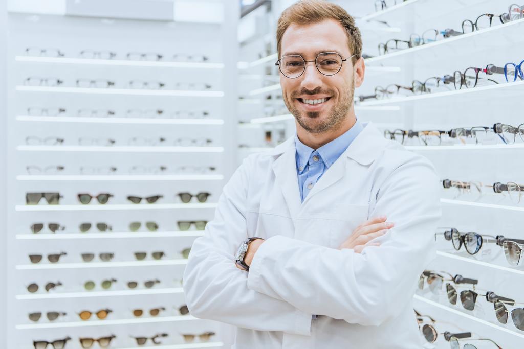 portrait of smiling professional optometrist in glasses posing with crossed arms in optica - Photo, Image
