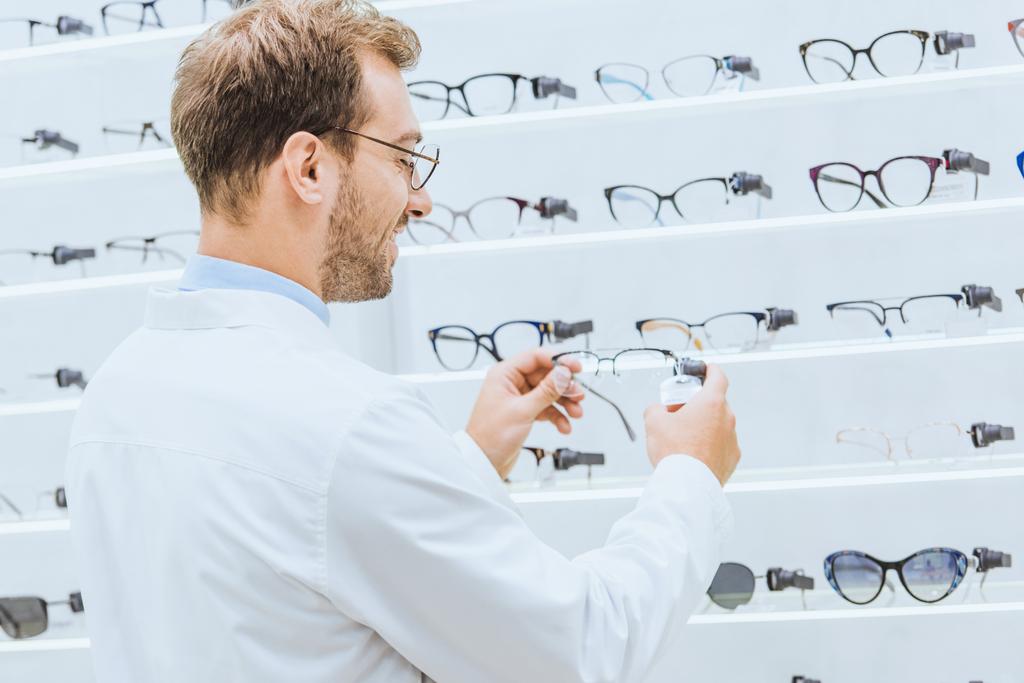 oculist nemen van brillen van planken in ophthalmic winkel - Foto, afbeelding
