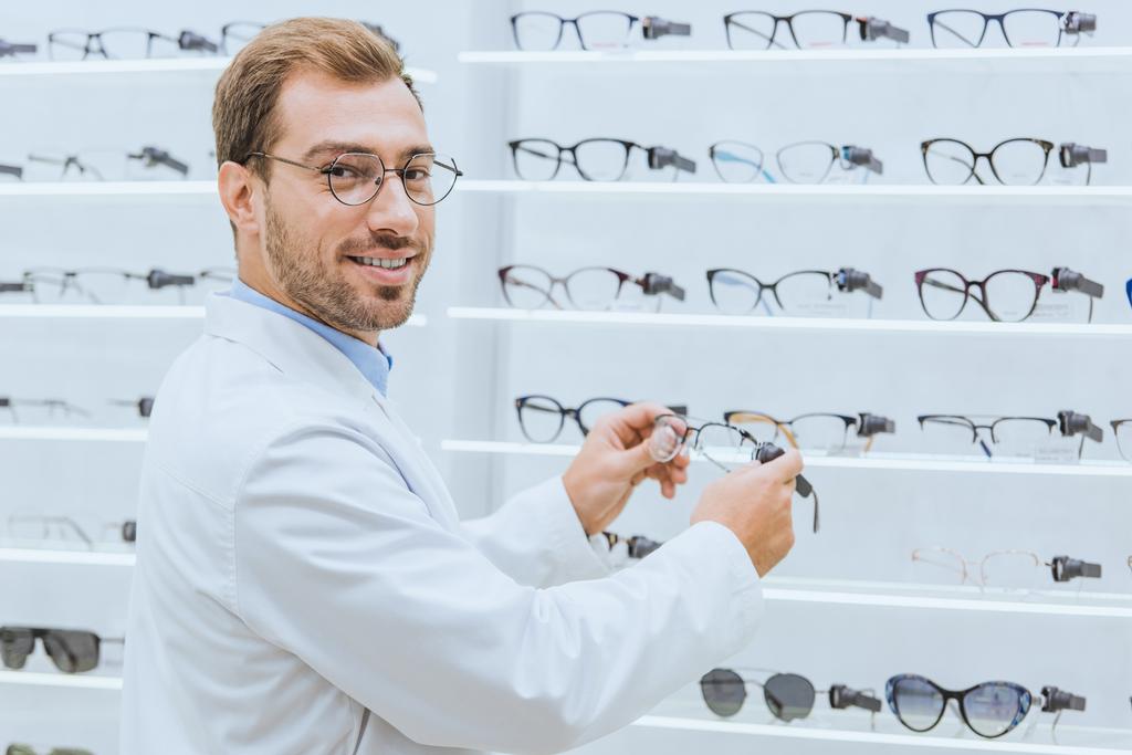 male optometrist taking glasses from shelves in ophthalmic shop - Photo, Image