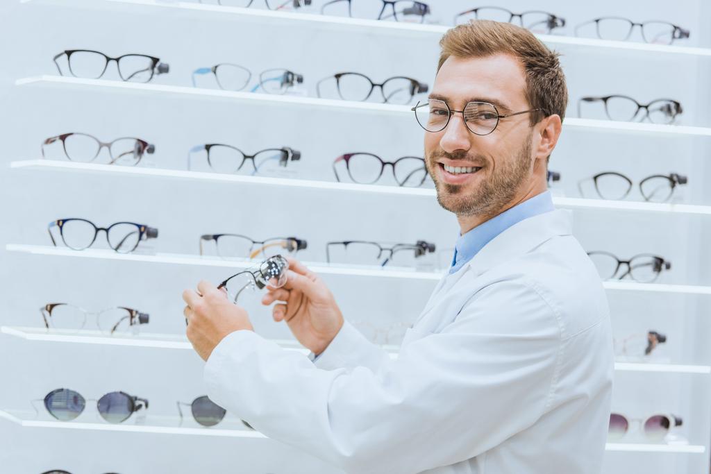 medico sorridente in cappotto bianco che prende gli occhiali dagli scaffali in ottica
 - Foto, immagini