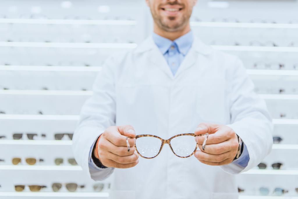 cropped view of oculist in white coat holding eyeglasses, selective focus - Photo, Image