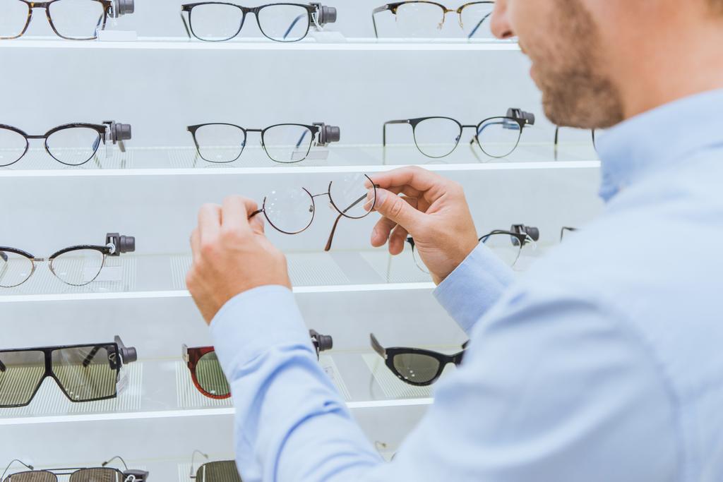 光学系の棚から眼鏡を取る人の部分的なビュー - 写真・画像
