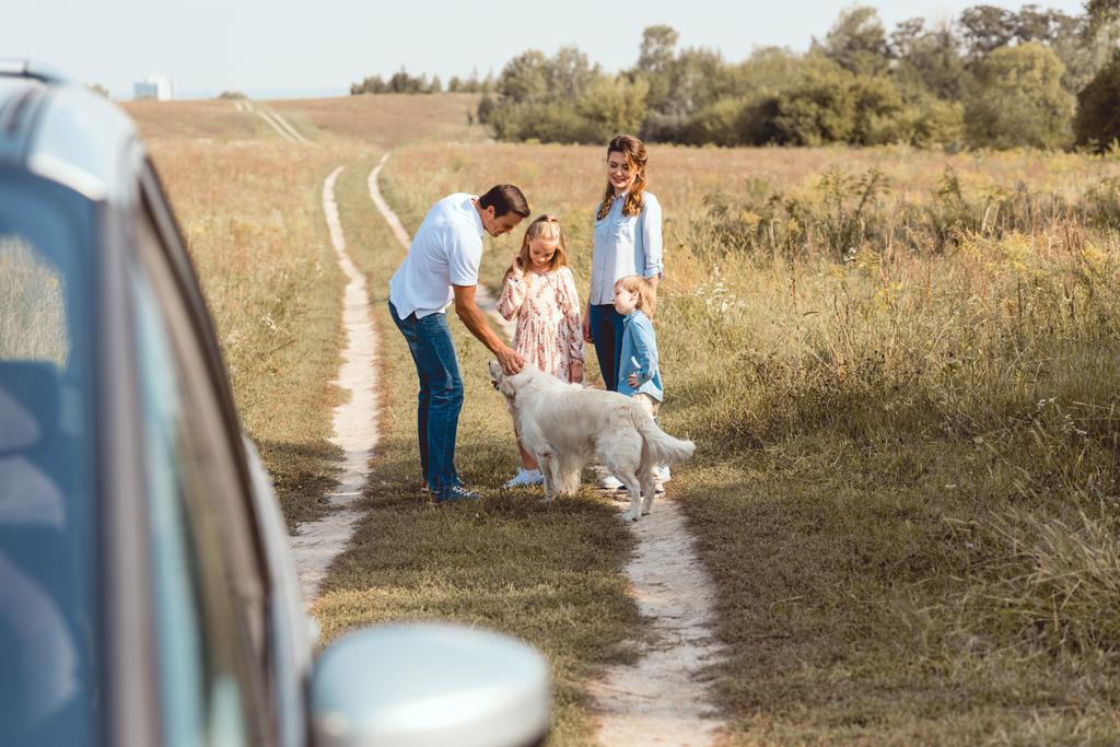 счастливая молодая семья с собакой-ретривером, проводящая время вместе в поле во время поездки на машине
 - Фото, изображение