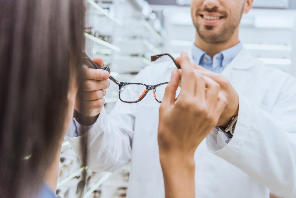 partial view of male oculist giving eyeglasses to woman in ophthalmic shop - Photo, Image