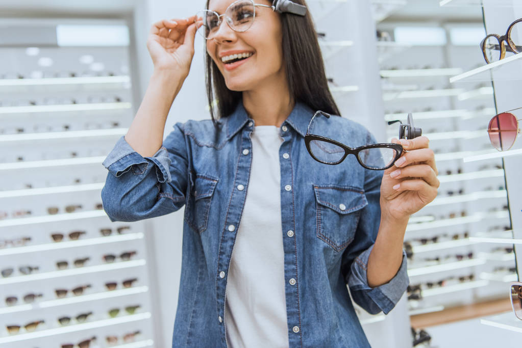 Selektiver Fokus der glücklichen jungen Frau, die sich für Brillen im Augengeschäft entscheidet - Foto, Bild