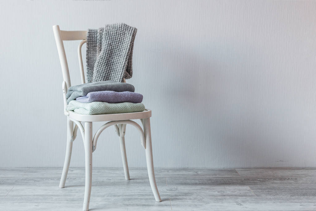 Stack of cozy knitted clothes on a wooden chair. Gray wall. Vintage tinting - Photo, Image