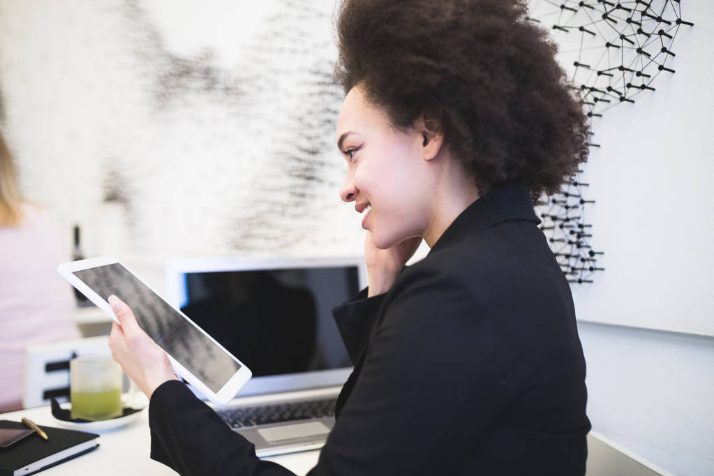 Femme d'affaires afro-américaine mignonne confiante et souriante assise dans un café moderne et utilisant son ordinateur portable ou sa tablette
. - Photo, image