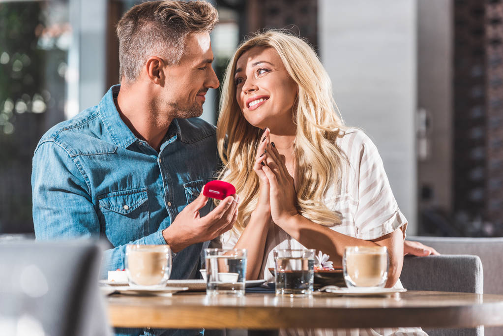 красивий хлопець пропонує щасливу дівчину і тримає червону кільцеву коробку в кафе
 - Фото, зображення