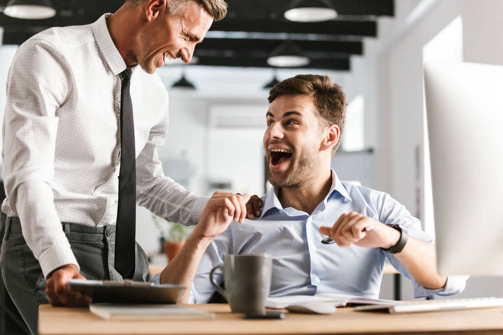 Зображення схвильованих здивованих шокованих щасливих емоційних чоловіків колег в офісі, що працюють з комп'ютером
. - Фото, зображення