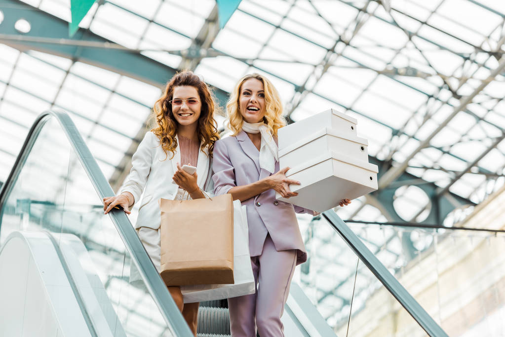 jeunes femmes à la mode avec des sacs à provisions et des boîtes sur l'escalator au centre commercial
 - Photo, image