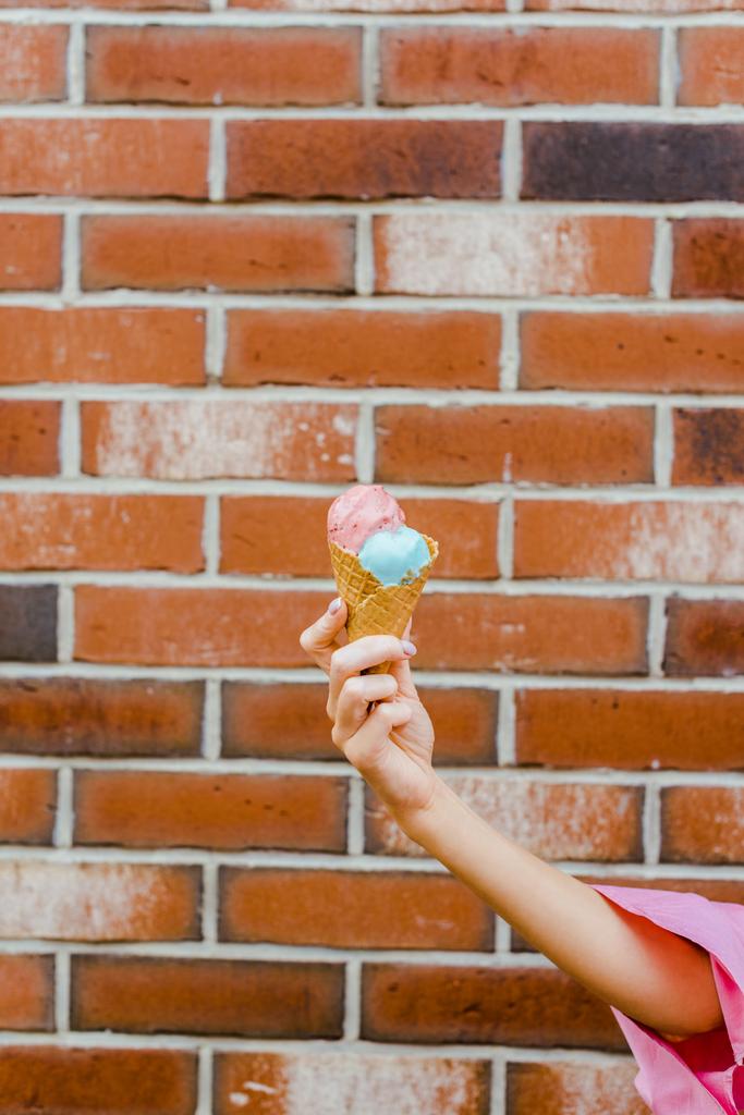 bijgesneden schot van vrouw bedrijf heerlijk ijs in wafel kegel voor bakstenen muur - Foto, afbeelding