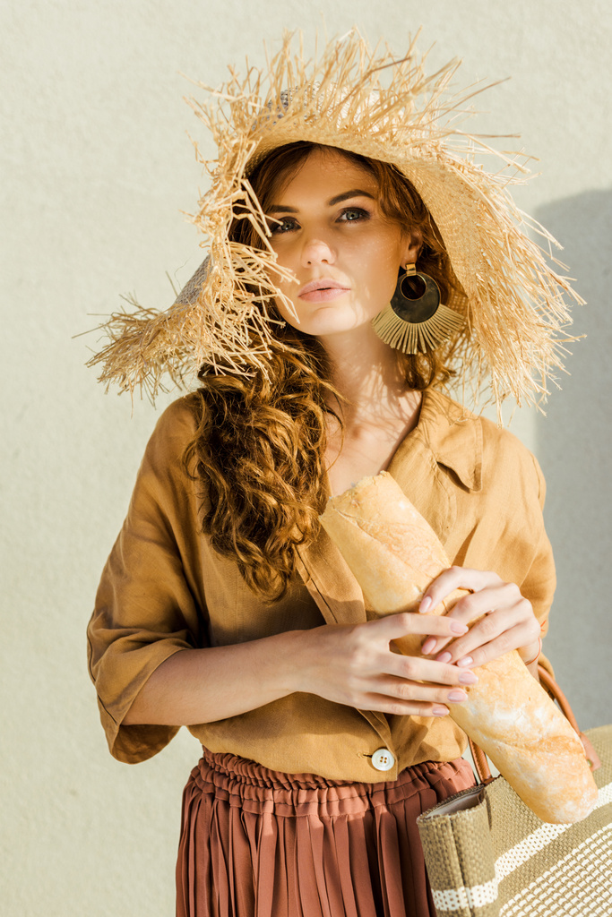 バゲット白い壁の前に立って、麦藁帽子でファッショナブルな美しい女性 - 写真・画像