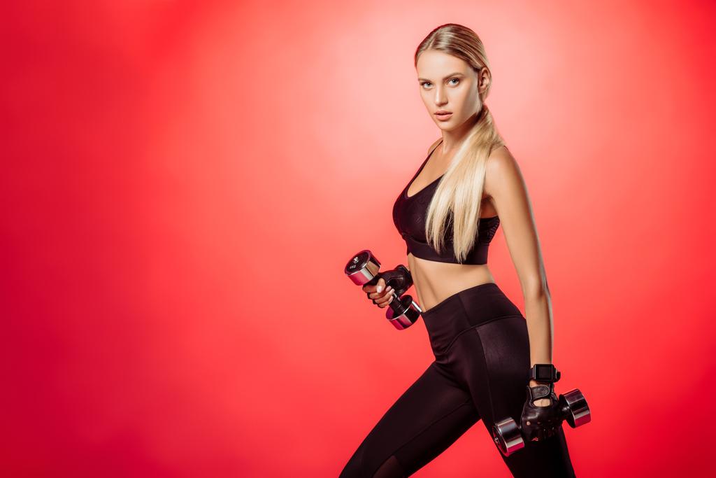 atraktivní sportovkyně trénink s činkami izolované na červenou a při pohledu na fotoaparát - Fotografie, Obrázek