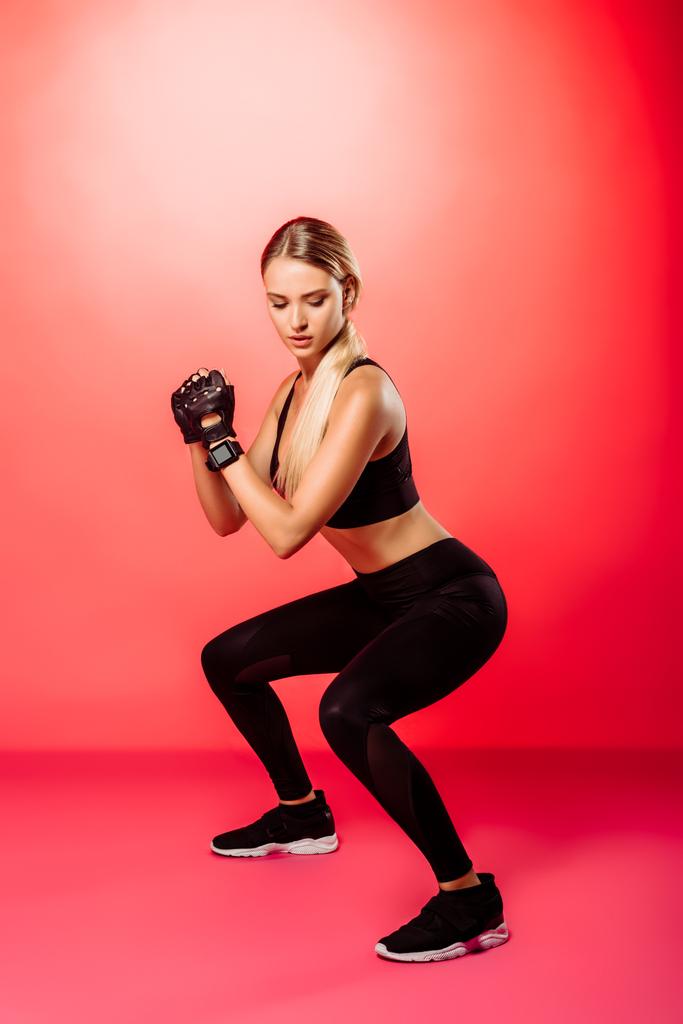 aantrekkelijke Sportvrouw opleiding en het doen squats op rood - Foto, afbeelding