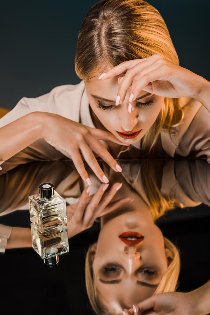stylish blond woman at mirror surface with perfume on dark background - Photo, Image