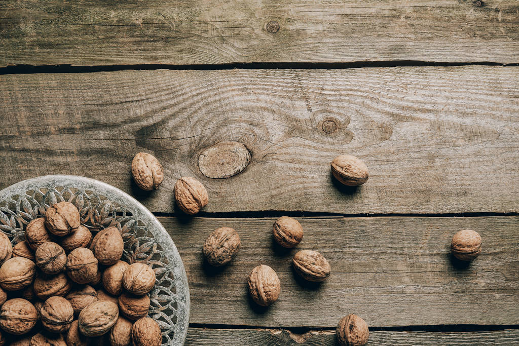top view of ripe organic walnuts and plate on wooden table - Photo, Image