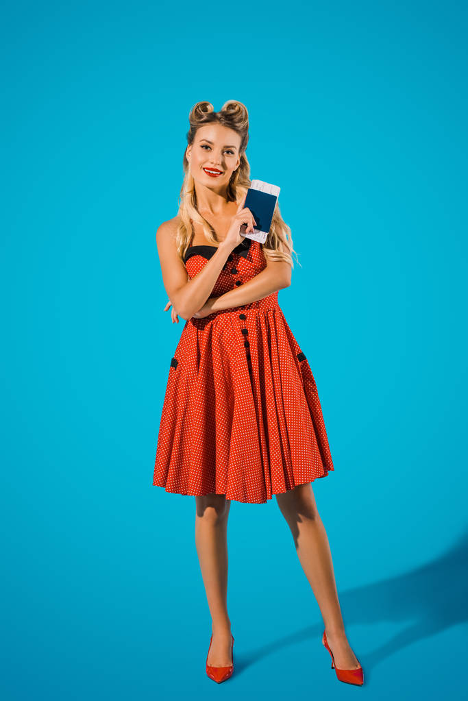 Lachende vrouw in pin-up stijl kleding met ticket en paspoort op blauwe achtergrond - Foto, afbeelding