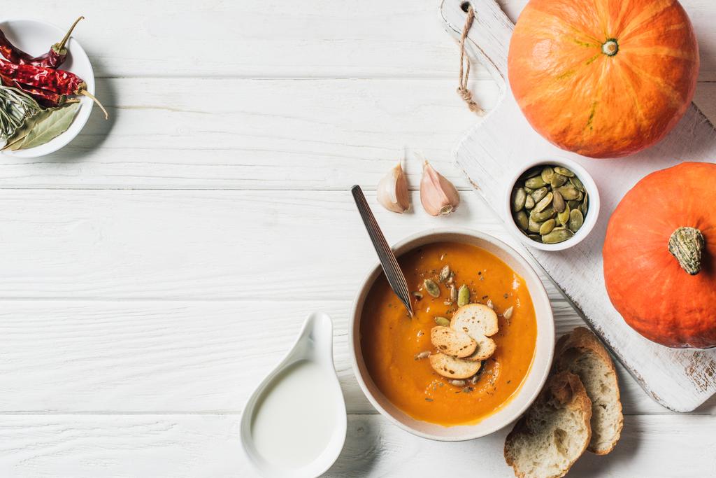 flat lay with pumpkins, garlic, rusks and bowl with homemade pumpkin cream soup on table  - Photo, Image