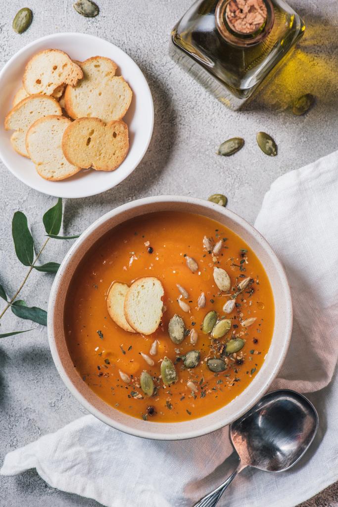 вид сверху на супы, бутылку оливкового масла и миску с тыквенным супом с семенами на столе
  - Фото, изображение