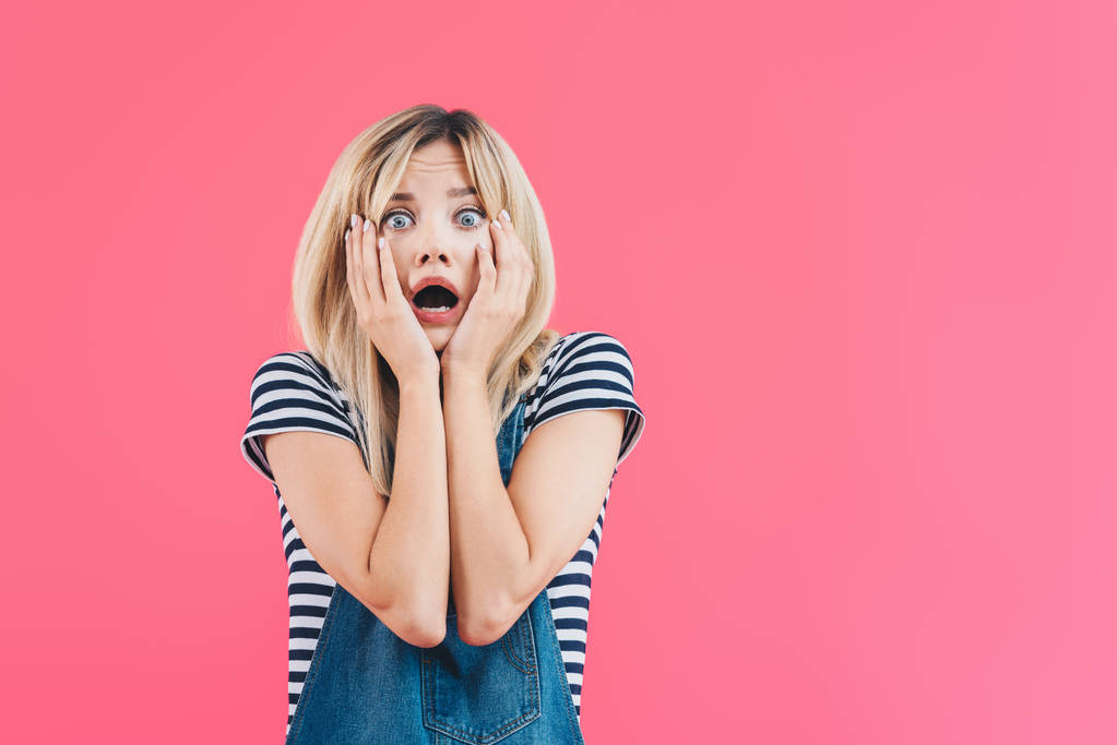 Shocked girl in denim overall touching face and looking at camera isolated on pink
 - Фото, изображение
