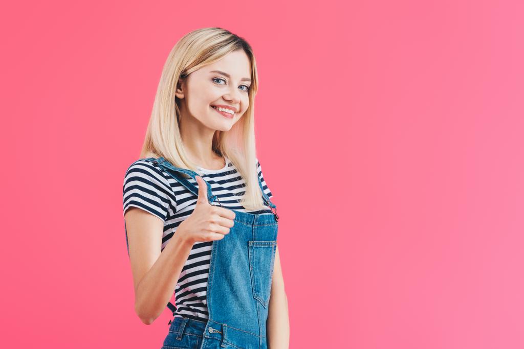 Lächeln schönes Mädchen in Jeans Overall zeigt Daumen nach oben isoliert auf rosa - Foto, Bild