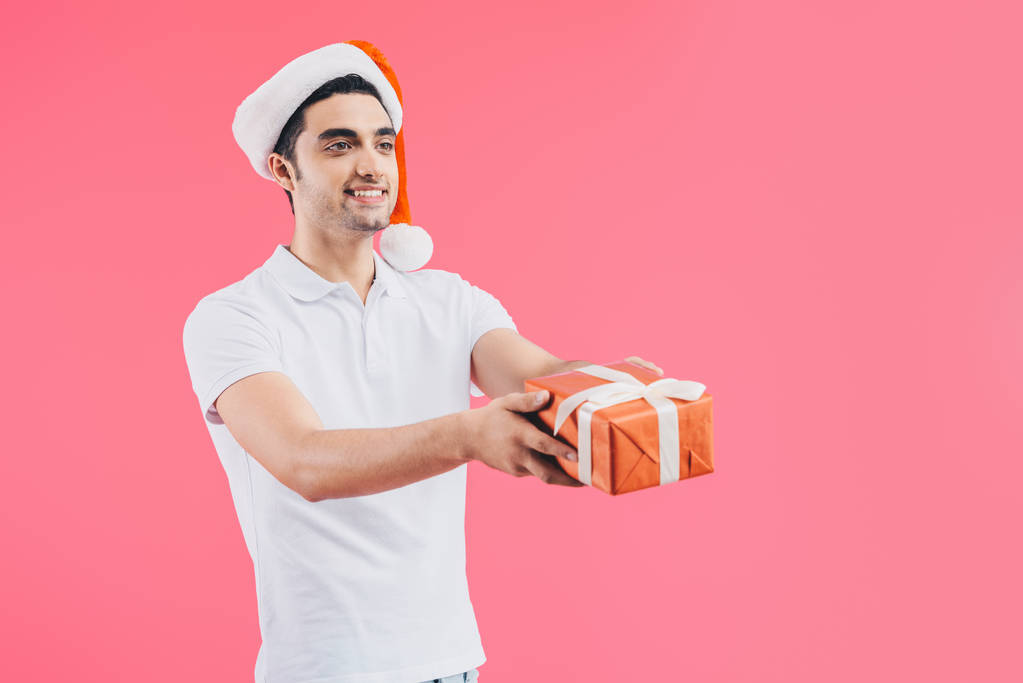 yakışıklı adam santa şapka hediye kutusu veren gülümseyen izole pembe, yeni yıl kavramı üzerinde - Fotoğraf, Görsel