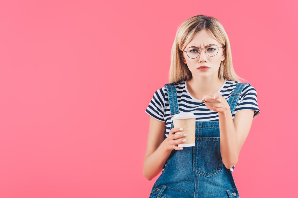 Portret van emotionele vrouw met koffie te gaan richten op camera geïsoleerd op roze - Foto, afbeelding