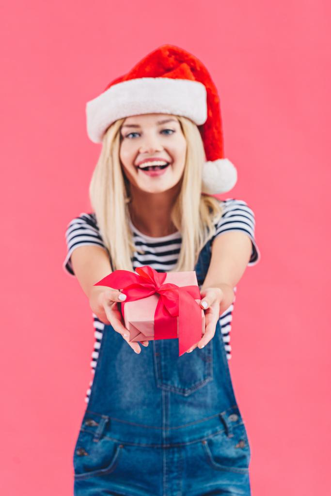 портрет молодої веселої жінки в капелюсі Санта Клауса, що тримає подарунок ізольовано на рожевому
 - Фото, зображення