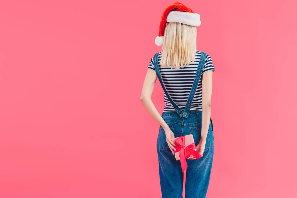 Rückansicht einer Frau mit Weihnachtsmann-Hut, die Geschenk isoliert auf rosa hält - Foto, Bild