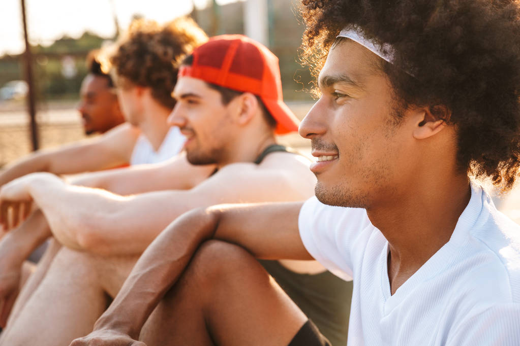 Εικόνα του όμορφος άνδρες παίκτες που κάθονται στο μπάσκετ παιδική χαρά εξωτερική και βλέποντας το παιχνίδι κατά τη διάρκεια του καλοκαιριού ηλιόλουστη μέρα - Φωτογραφία, εικόνα