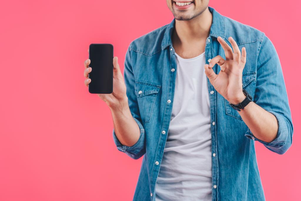 Teilbild eines jungen Mannes, der ok Zeichen macht und zeigt Smartphone mit leerem Bildschirm isoliert auf rosa - Foto, Bild