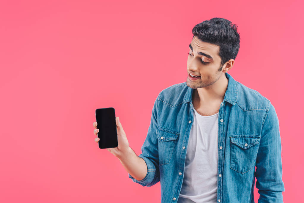 joven sonriente mostrando teléfono inteligente con pantalla en blanco aislado en rosa
 - Foto, Imagen