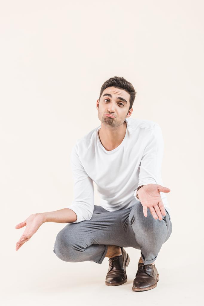 disappointed young man crouching and looking at camera isolated on beige - Photo, Image
