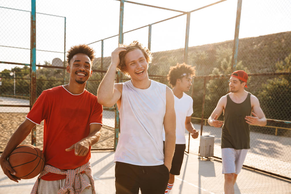 Фото мускулистых спортсменов, улыбающихся и держащих мяч, стоя на баскетбольной площадке под открытым небом в летний солнечный день
 - Фото, изображение