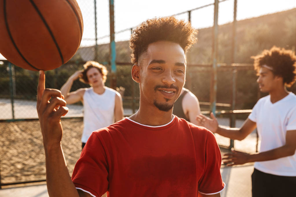 Portret van jonge sportieve mannen spelen basketbal op de speeltuin buiten en Amerikaanse jongen draaiende bal aan zijn vinger - Foto, afbeelding