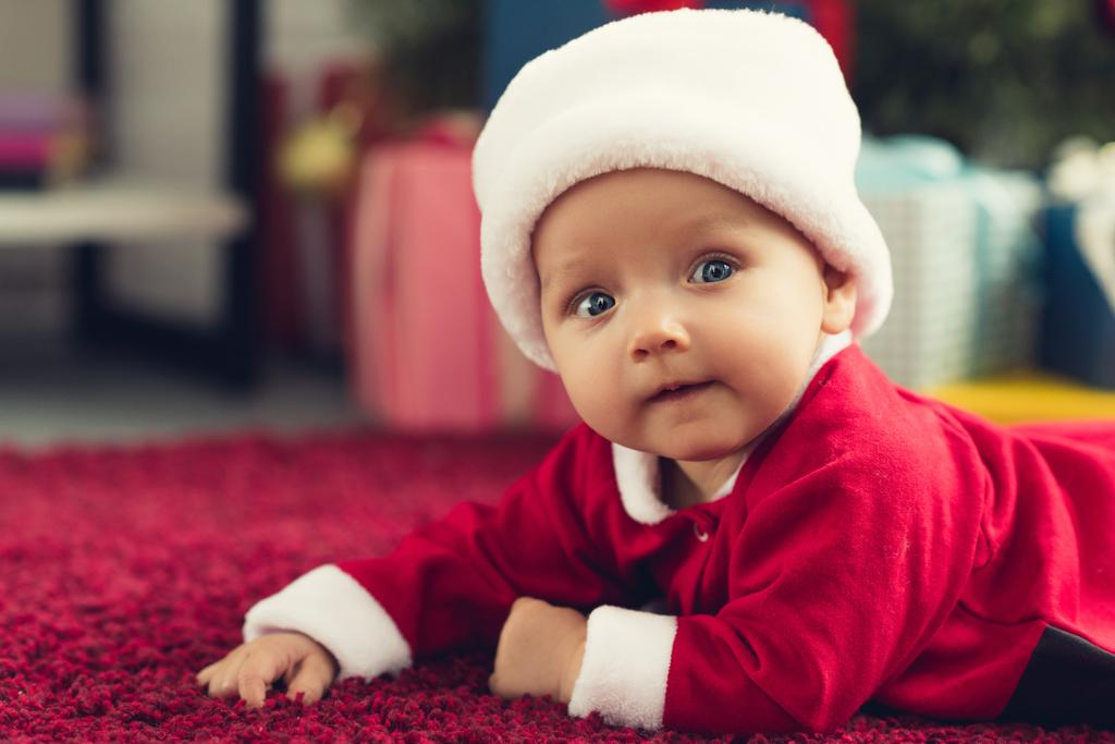 close-up portrait of adorable little baby in santa hat lying on floor and looking at camera - Photo, Image