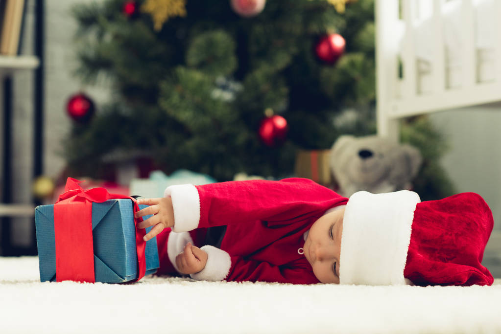 aranyos kis baba a santa ruha feküdt a padlón és karácsonyi ajándék doboz - Fotó, kép