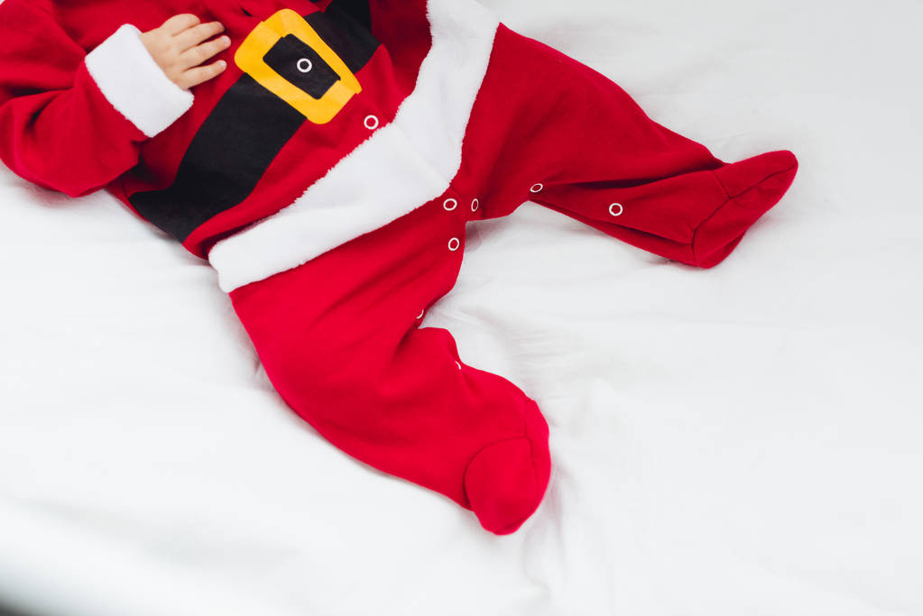 обрезанный снимок маленького ребенка в костюме Санты, лежащего в постели
 - Фото, изображение