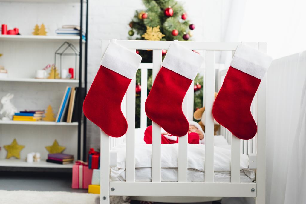 chaussettes cadeaux suspendues au lit bébé avec petit bébé en costume de Père Noël à l'intérieur
 - Photo, image