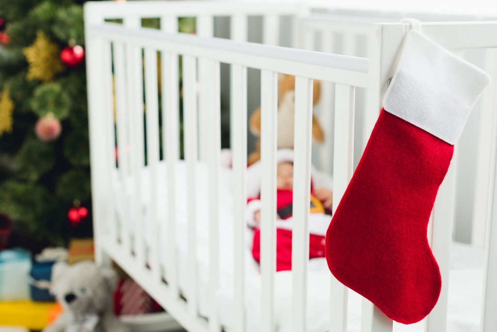 前景にクリスマスのギフトのソックス付きのベビーベッドに横たわっているサンタ服の小さい赤ん坊 - 写真・画像