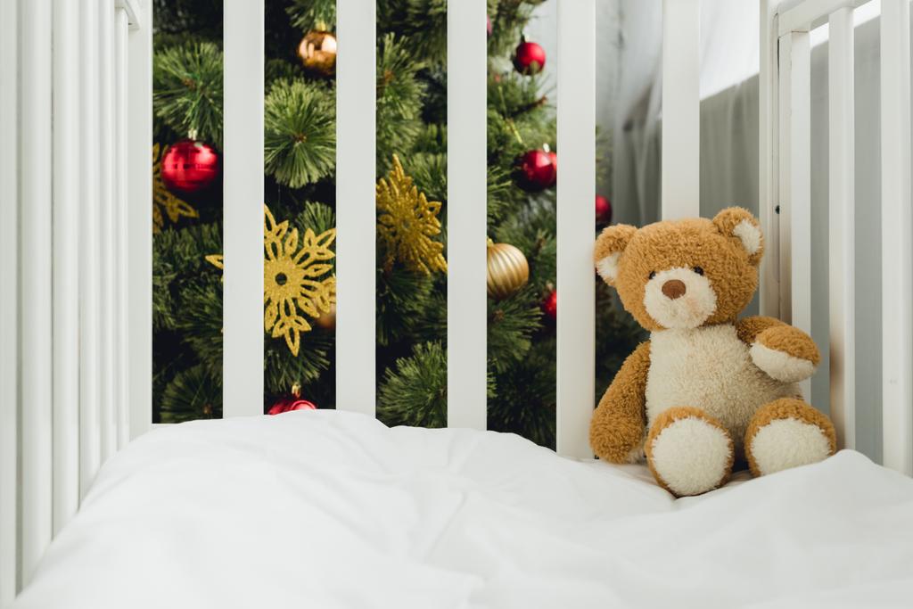ursinho de pelúcia na cama infantil na frente da árvore de natal
 - Foto, Imagem