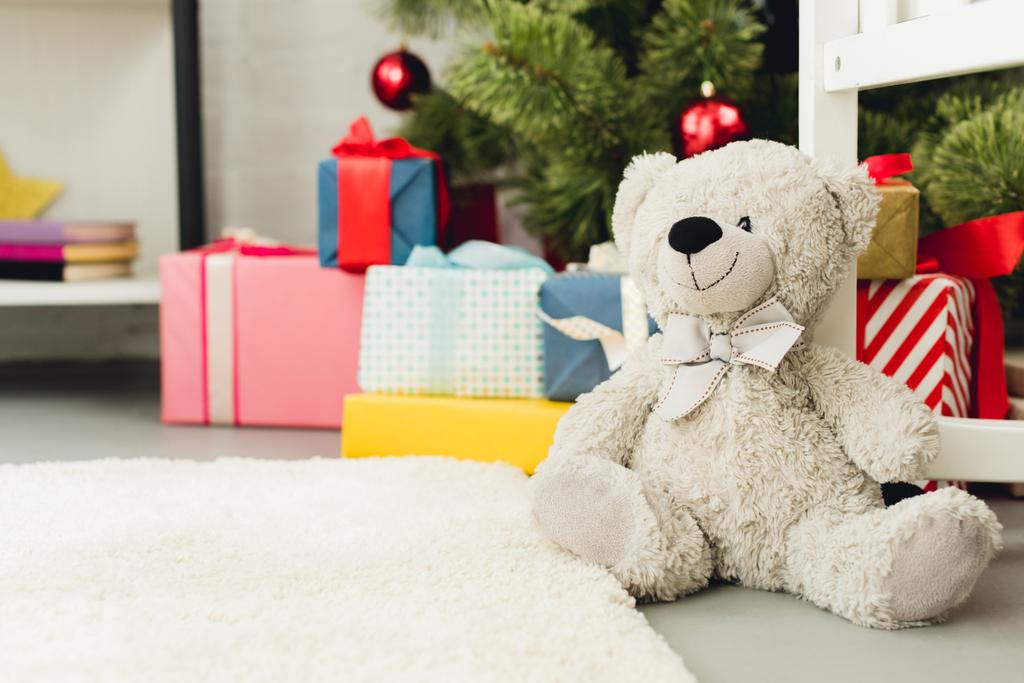 close-up shot of teddy bear leaning on cradle in front of christmas tree and gifts - Photo, Image