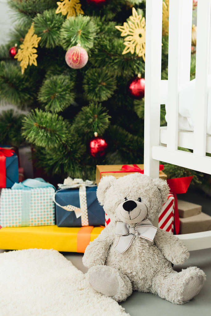 Medvídek, opíraje se o kolébku před vánoční stromek a dárky - Fotografie, Obrázek