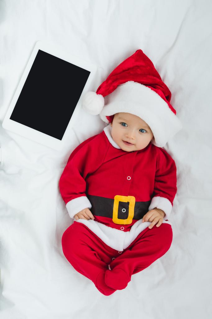 κάτοψη του χαρούμενος λίγο μωρό σε santa κοστούμι ξαπλωμένη στο παχνί με tablet - Φωτογραφία, εικόνα