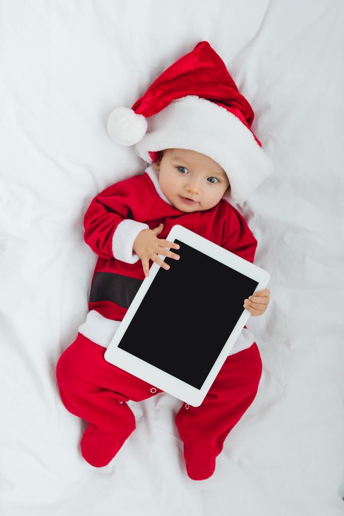 κάτοψη του αξιολάτρευτο μωράκι σε santa κοστούμι ξαπλωμένη στο παχνί με tablet - Φωτογραφία, εικόνα
