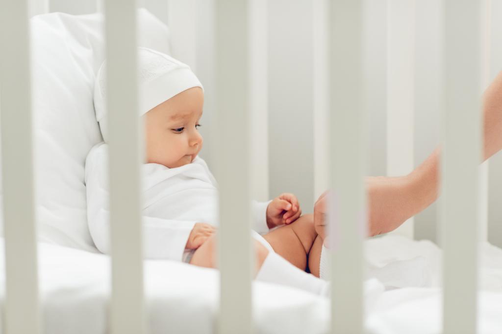 schattige kleine baby in witte hoed zitten in wieg - Foto, afbeelding