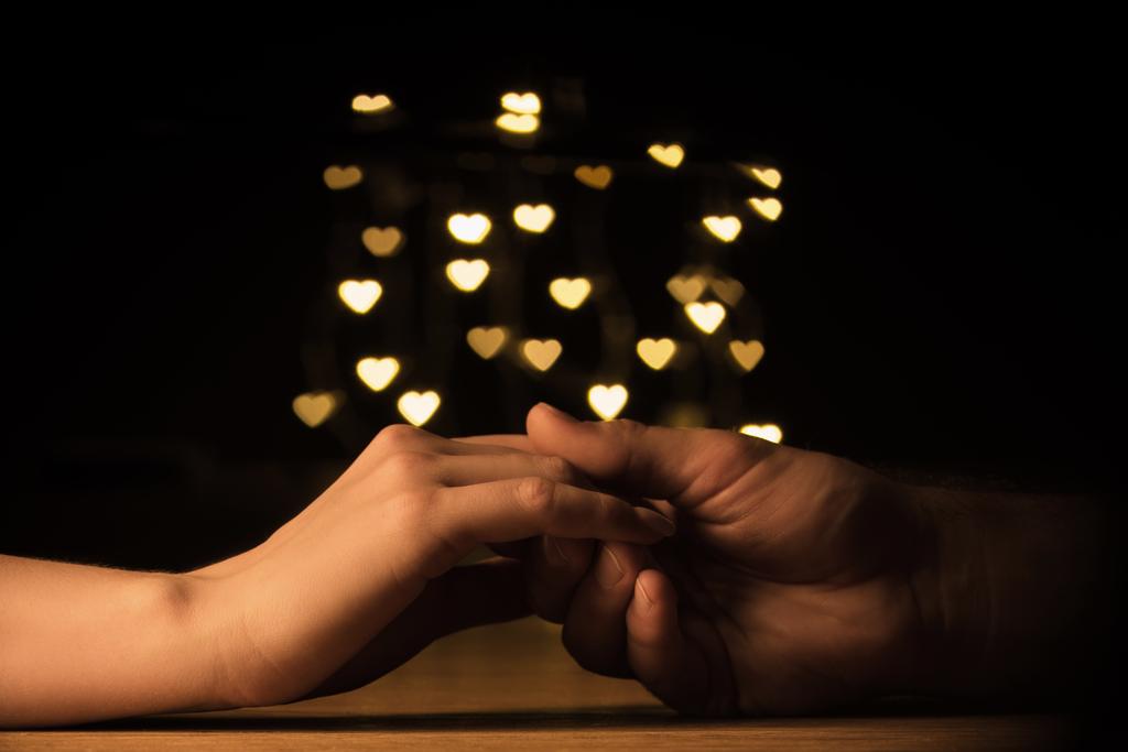 cropped shot of couple holding hands with hearts bokeh background - Photo, Image